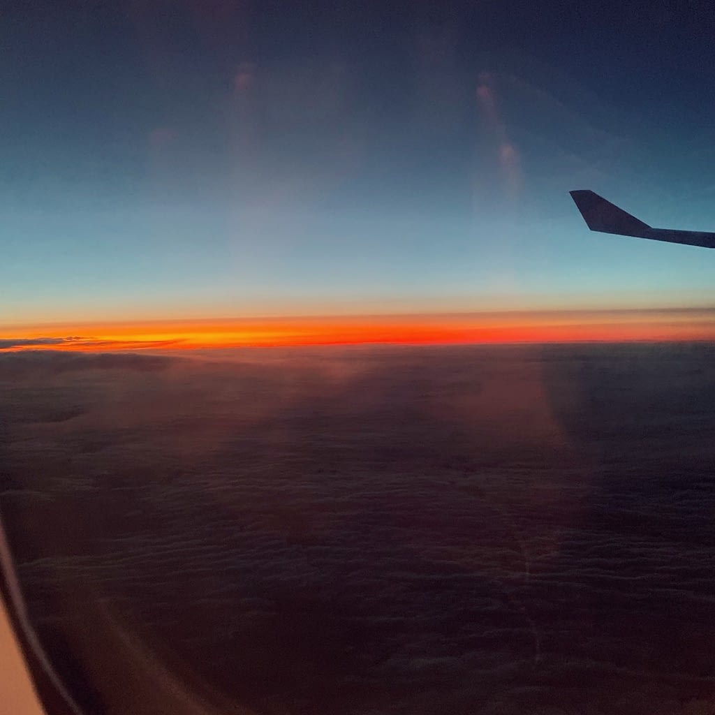 Airplane window view, orange sunset against blue sky