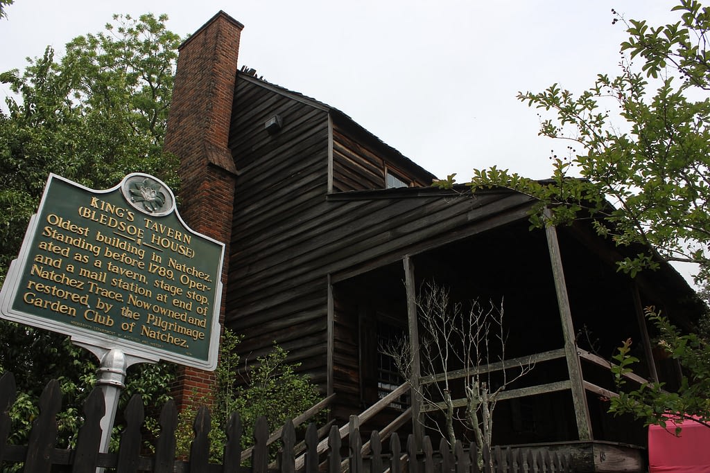 Building made of dark wood with brick chimney, green King's Tavern sign