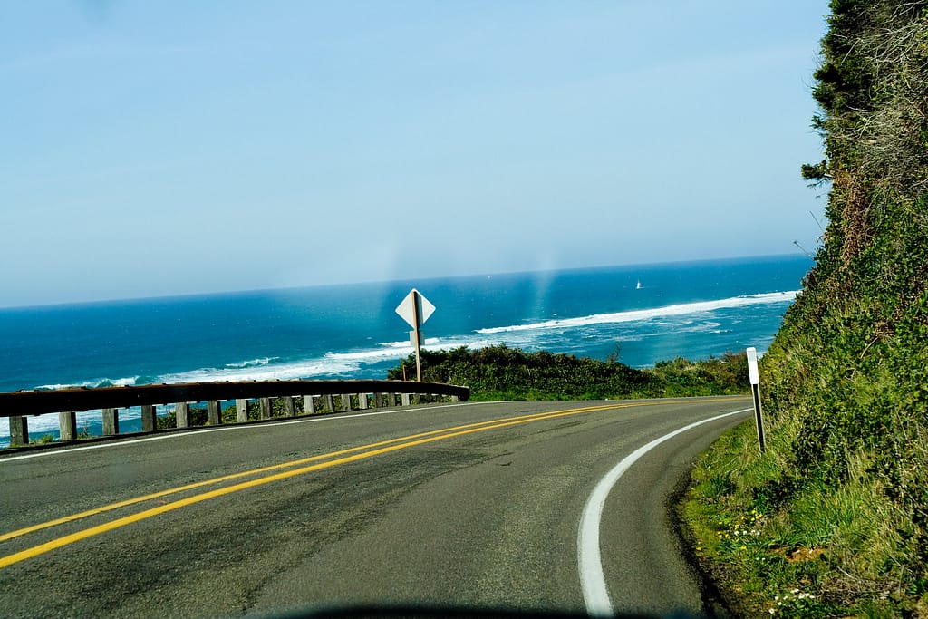 Curving road with blue sky and ocean ahead, view from interior of car