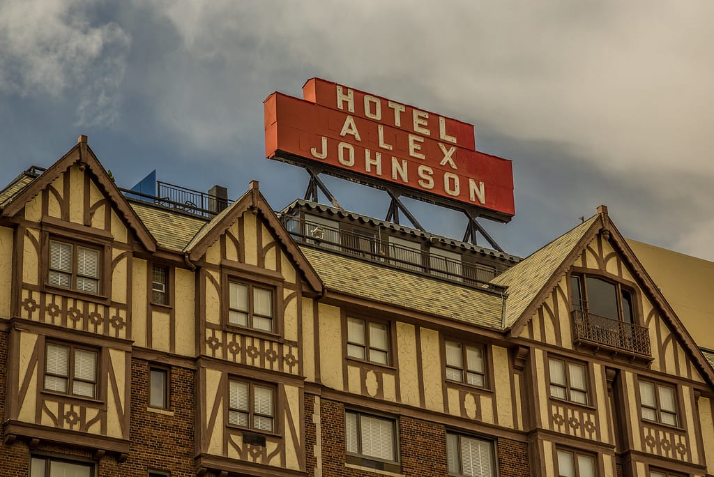 Close-up of red Hotel Alex Johnson sign on top of brick and yellow building