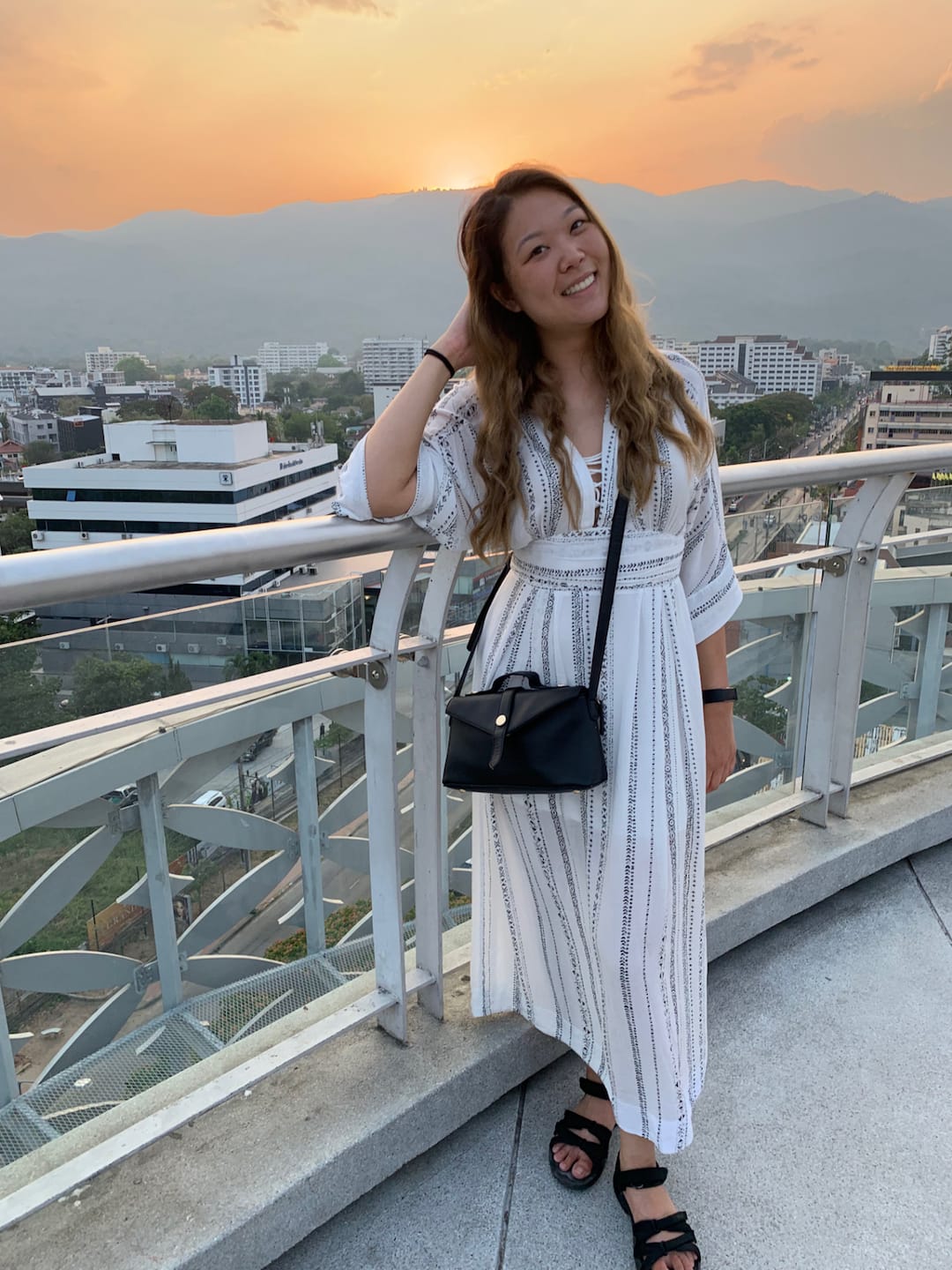 Girl wearing a white dress, smiling with mountains and an orange sunset behind her