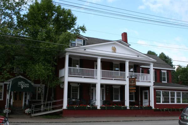 Brick and white building on street with green awning that reads The Green Mountain Inn